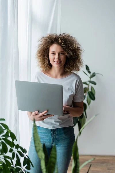 Szczęśliwa Kręcona Kobieta Stojąca Laptopem Domu Patrząca Kamerę — Zdjęcie stockowe