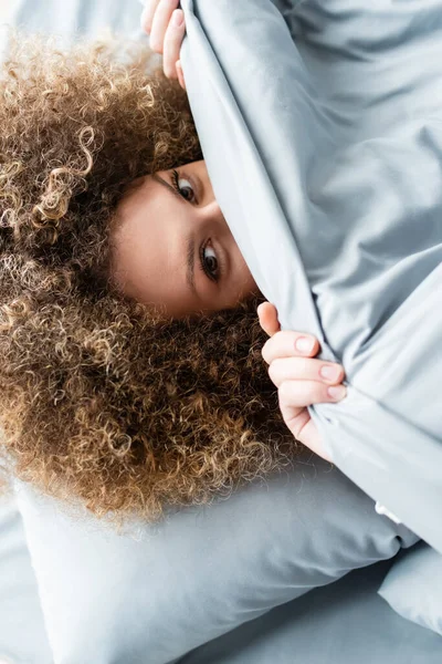 Top View Curly Woman Obscuring Face Blanket Looking Camera — Stock Photo, Image