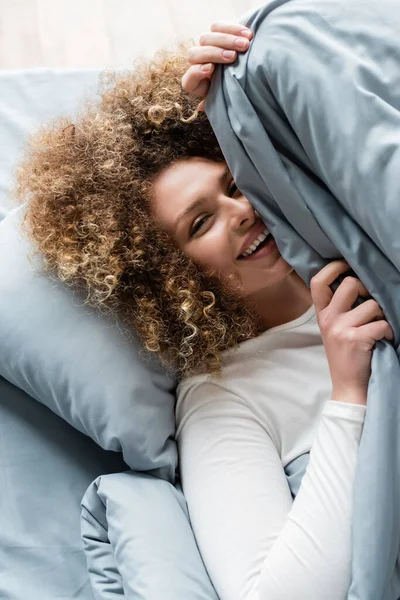 Cheerful Curly Woman Looking Camera While Hiding Grey Blanket — Stock Photo, Image