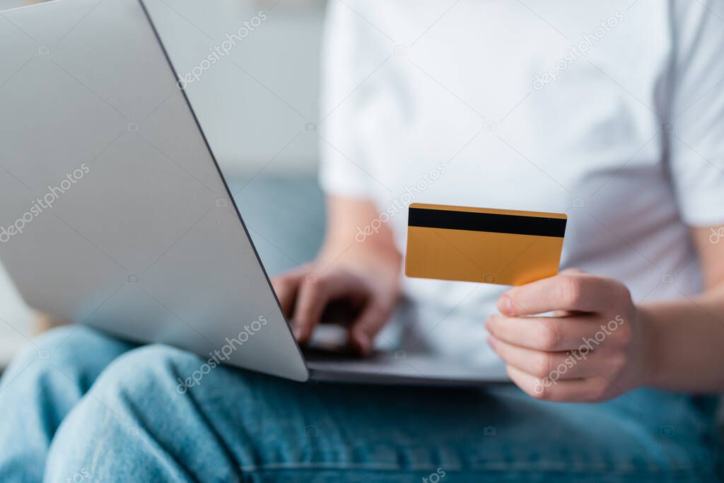 partial view of woman with credit card using laptop on blurred background