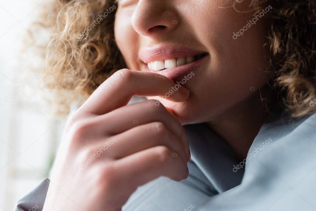 partial view of smiling woman with wavy hair holding hand near chin