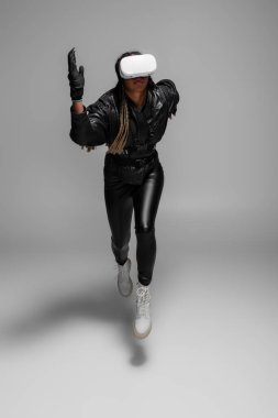 African american woman in leather gloves and vr headset running on grey background  clipart