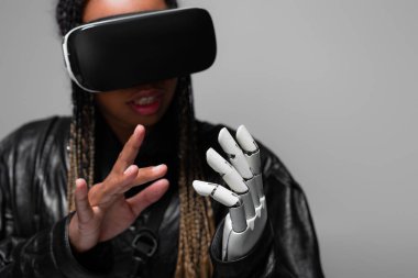 VR kulaklıklı Afrikalı Amerikalı kadın. Robotik elleri gri renkte. 