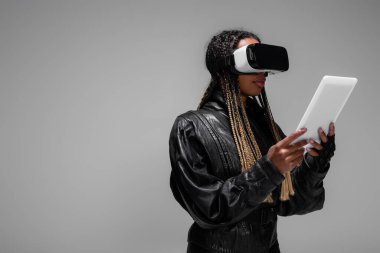 VR kulaklıklı şık Afro-Amerikan kadın elinde dijital tablet gri üzerinde izole edilmiş. 