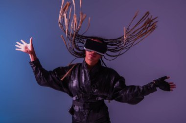 Saçları örgülü, mavi ve mor arka planda vr kulaklık kullanan şık Afro-Amerikan kadın. 