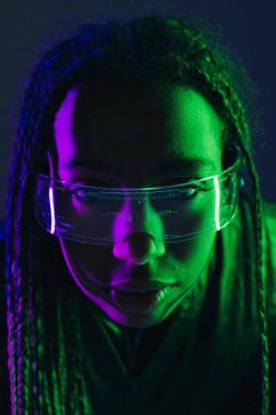 Portrait of african american woman with pigtails using smart glasses isolated on dark blue  clipart