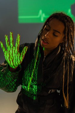 Gri arka planda bilgisayar kodu yansıması olan deri ceketli Afrikalı Amerikalı kadın. 