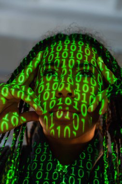 Gri arka planda bilgisayar kodu yansıtması olan Afrikalı Amerikalı kadının düşük açılı görüntüsü 