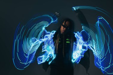 Beyaz gözlüklü şık Afro-Amerikalı kadın gri arka planda neon ışıkların yanında poz veriyor. 