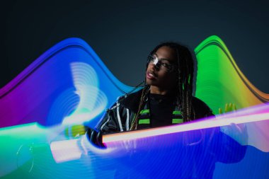 Beyaz arka planda neon çubukla poz veren akıllı gözlüklü Afro-Amerikan kadın. 