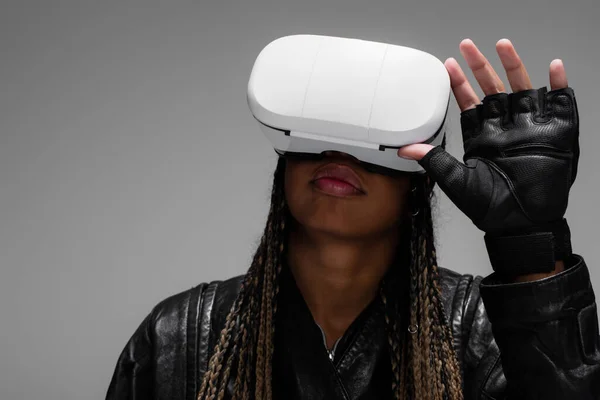 African american woman in leather glove using vr headset isolated on grey