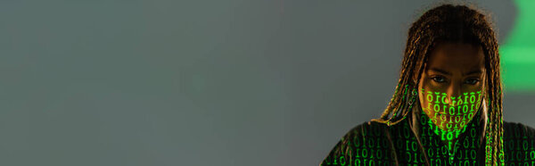 African american woman with binary code on face looking at camera on grey background, banner 