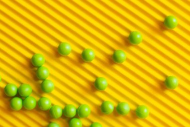 top view of small green balls scattered on textured yellow background clipart