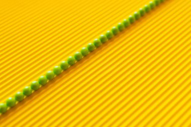 top view of diagonal line of small green balls on yellow corrugated background clipart