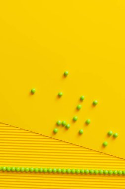 top view of green beads scattered on yellow textured background clipart