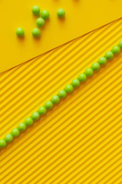 top view of line and scattering of green balls on textured yellow background clipart