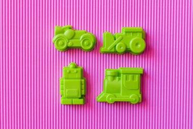 Mor desenli arka planda plastik araçların yanındaki yeşil oyuncak robotun üst görüntüsü