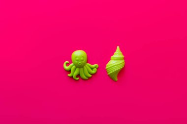 top view of green octopus and shellfish toys on pink background clipart