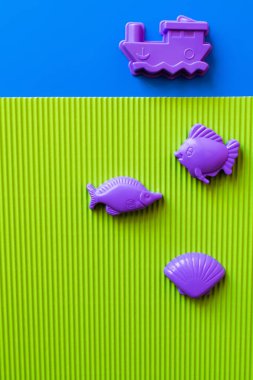 top view of purple sea animals and vessel toys on blue and green background clipart