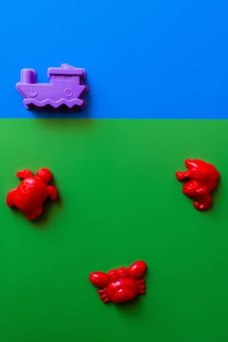 top view of red sea animals and purple ship toys on blue and green background clipart
