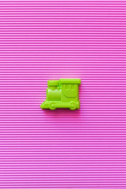 top view of bright green toy locomotive on violet textured background clipart