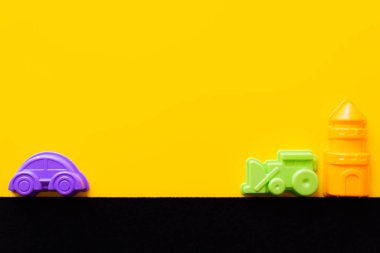 top view of toy tower near colorful plastic vehicles on black and yellow background clipart
