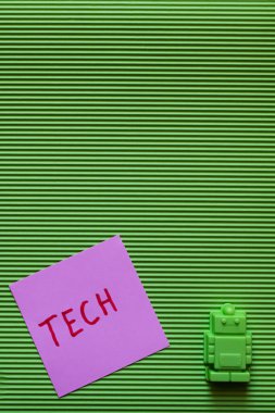 Yeşil desenli arka planda teknolojik harflerle mor kağıdın yanındaki plastik oyuncak robotun üst görüntüsü
