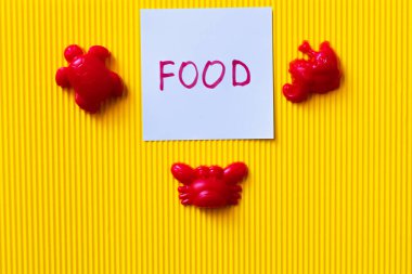top view of red toy sea creatures near blue card with food lettering on yellow background clipart