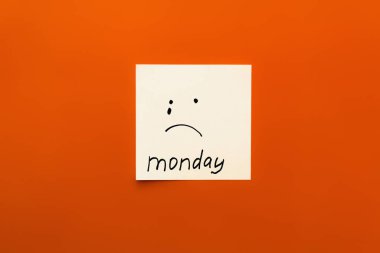 top view of paper note with crying emoticon and monday lettering on orange background clipart
