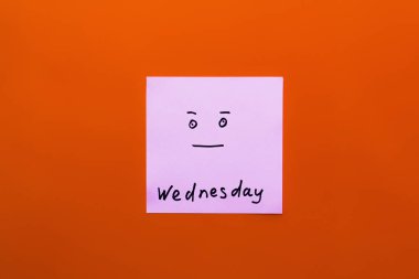 top view of paper note with wednesday lettering and calm smiley on orange background clipart