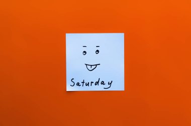 top view of sticky note with saturday inscription and sticking out tongue emoji on red background clipart
