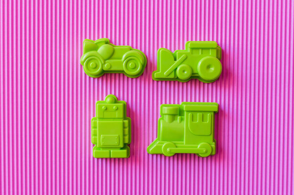 вид на зеленый игрушечный робот рядом с пластиковыми транспортными средствами на фиолетовом фоне