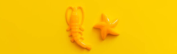 top view of starfish and shrimp toys on bright yellow background, banner