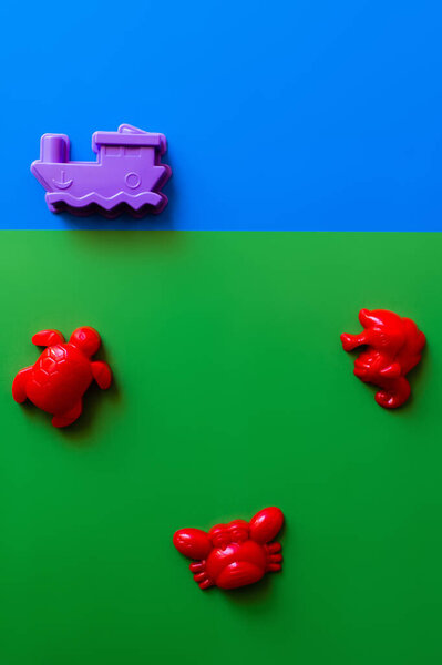 top view of red sea animals and purple ship toys on blue and green background