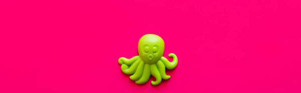 top view of bright green octopus toy on pink background, banner