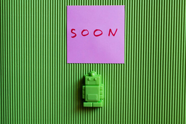 верхний вид игрушечного робота рядом с фиолетовой бумагой с надписью на зеленом текстурированном фоне