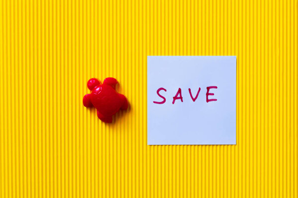 top view of red toy turtle near paper with save lettering on textured yellow background