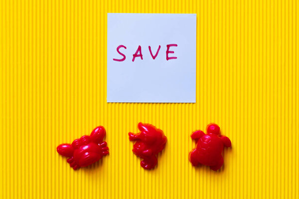 top view of toy sea animals near blue paper with save lettering on yellow background