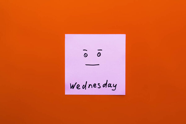 top view of paper note with wednesday lettering and calm smiley on orange background