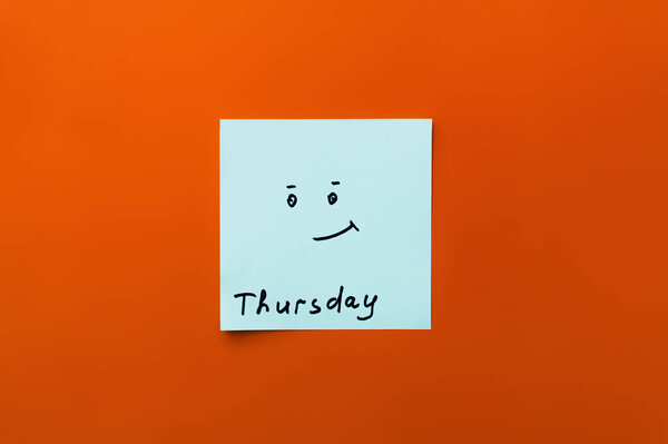 top view of sticky note with thursday inscription and positive smiley on orange background