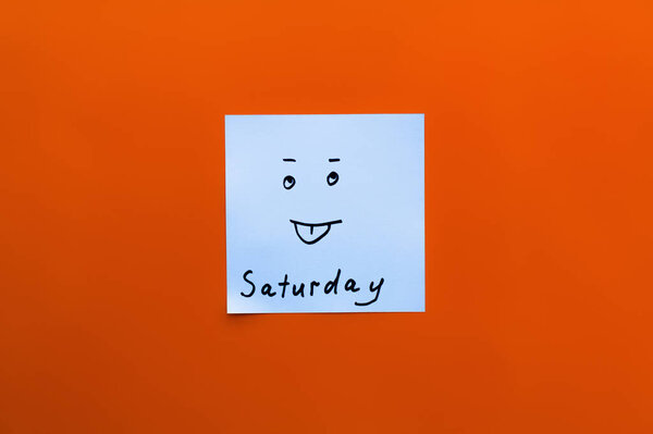 top view of sticky note with saturday inscription and sticking out tongue emoji on red background