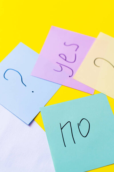 top view of paper notes with question mark near yes and no lettering on yellow background