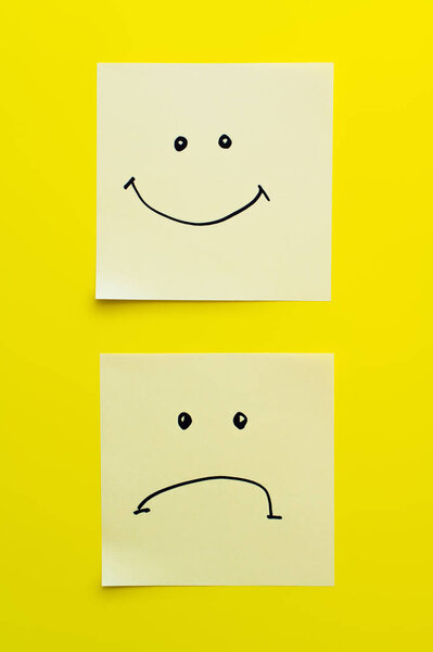 top view of sticky notes with joyful and sad smileys on bright yellow background