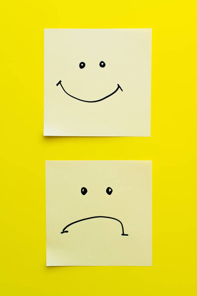 верхний вид липких нот с радостными и грустными улыбками на ярко-желтом фоне