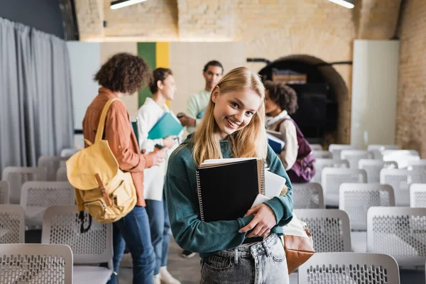 Grazioso Studente Con Copybooks Sorridente Macchina Fotografica Vicino Interrazziale Compagni — Foto Stock