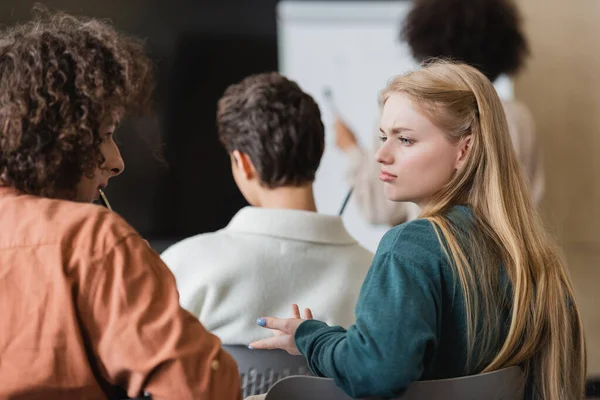 discouraged woman talking to classmate in university classroom