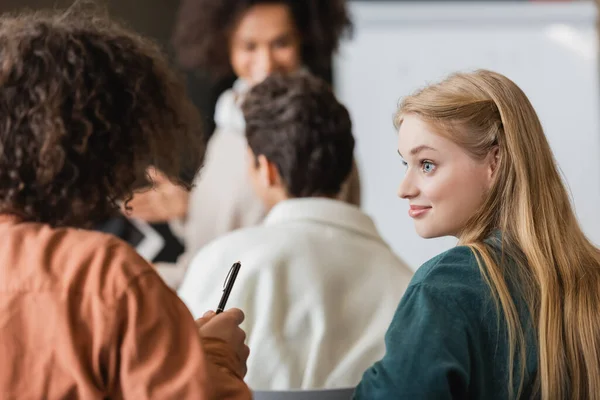 Fröhlicher Student Schaut Lockige Freundin Die Mit Stift Klassenzimmer Sitzt — Stockfoto