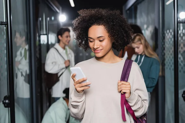 Sırt Çantalı Akıllı Telefonlu Genç Afro Amerikan Kadın Üniversite Koridorunda — Stok fotoğraf