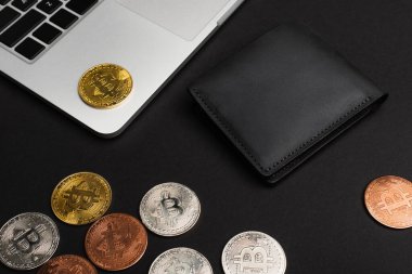 KYIV, UKRAINE - 26 Nisan 2022: Cüzdan yakınındaki bitcoins ve siyah arkaplan üzerindeki laptop yüksek açılı görünüm