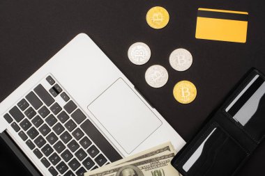 KYIV, UKRAINE - 26 Nisan 2022: Bilgisayarlı ve siyah arkaplanda bitcoins olan kredi kartı yakınındaki dolarların üst görünümü